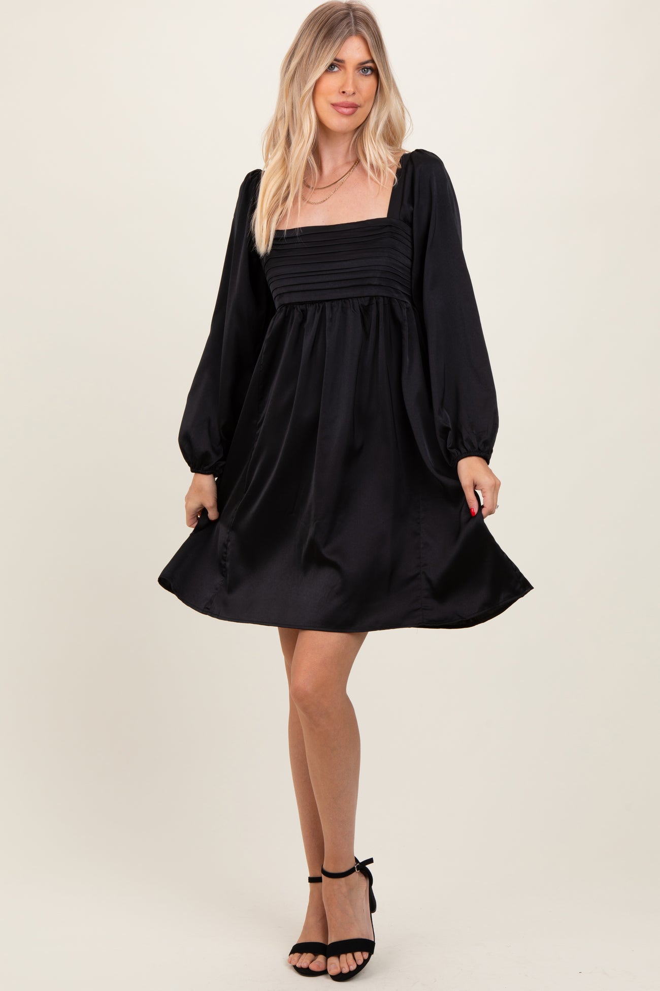 woman wearing a black satin puff sleeve mini dress with a square neckline and a fitted bodice
