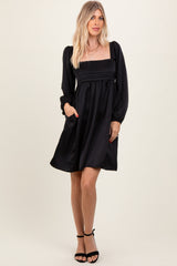 woman wearing a black puff sleeve mini dress with a square neckline and side pockets