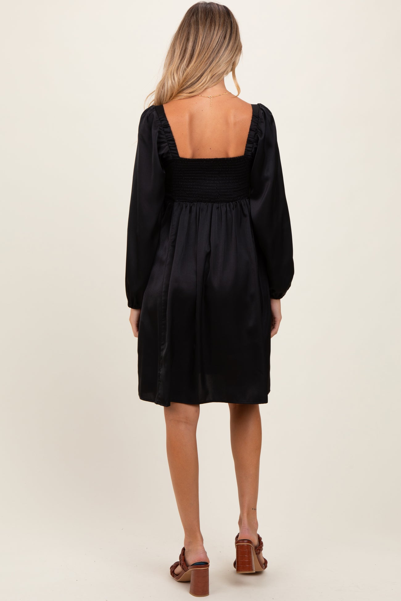 woman wearing a black maternity dress with a smocked back and puff sleeves, showing her back view