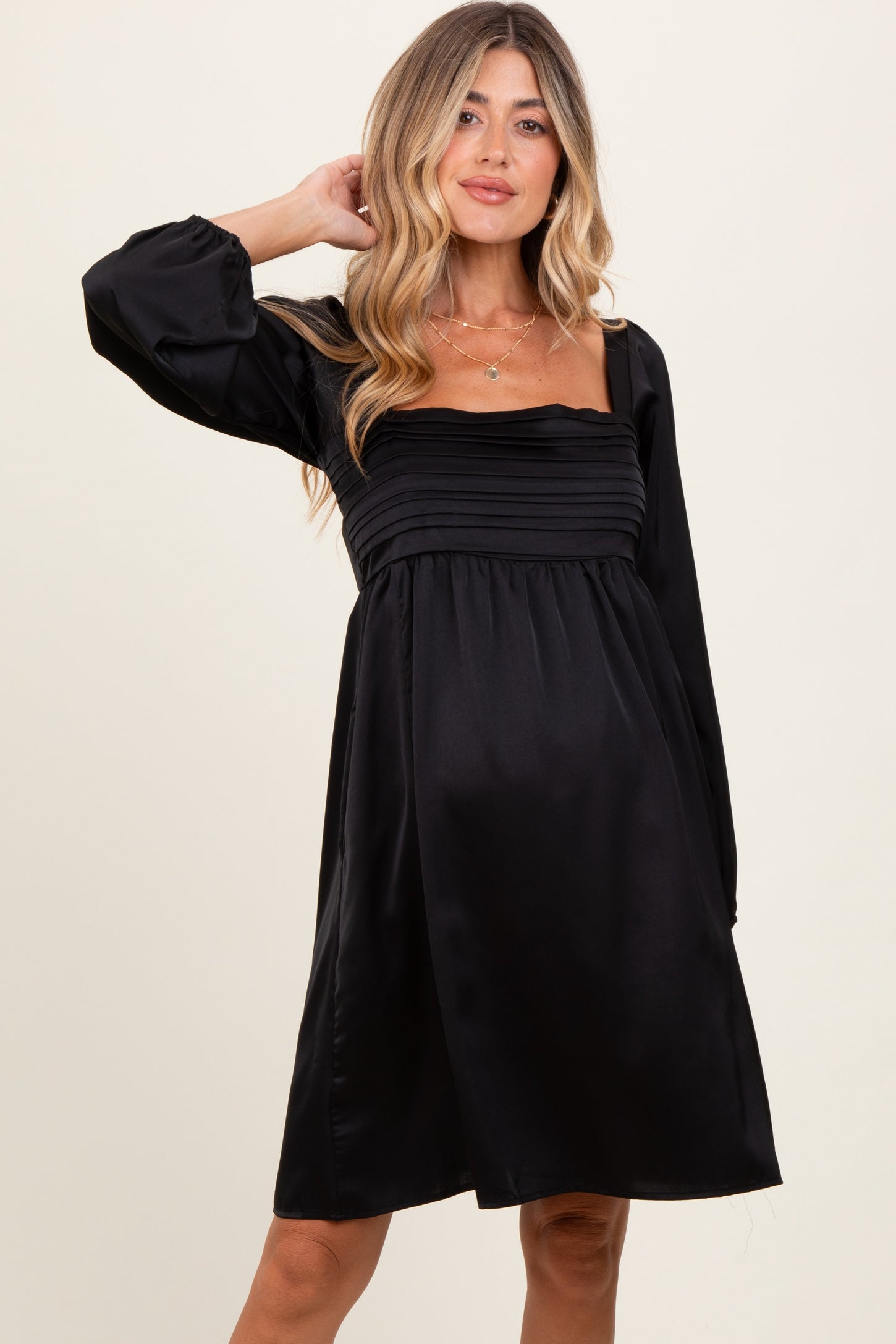 woman wearing a black maternity dress with puff sleeves and a square neckline, showcasing her baby bump