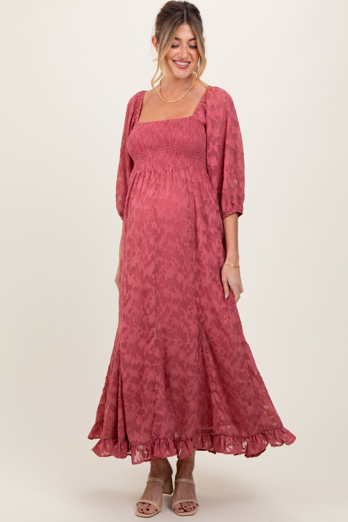 woman wearing a pink smocked maternity dress with puff sleeves and ruffled hem, highlighting her baby bump