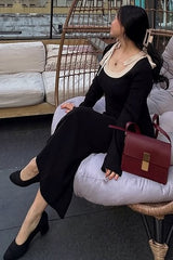 woman sitting on a chair wearing a black long sleeve dress with a cream collar and holding a burgundy handbag