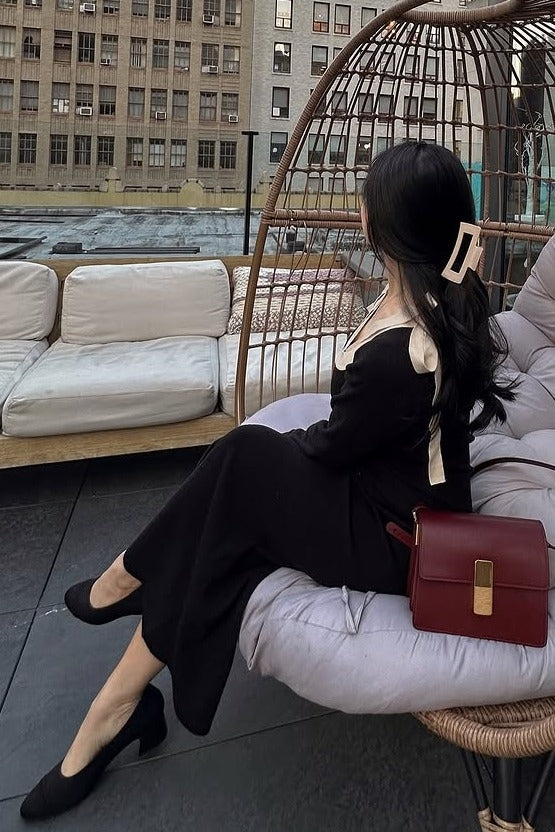 woman wearing a black dress with a cream-colored collar and a large hair clip, sitting in a woven chair outdoors