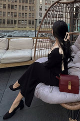 woman wearing a black dress with a cream-colored collar and a large hair clip, sitting in a woven chair outdoors
