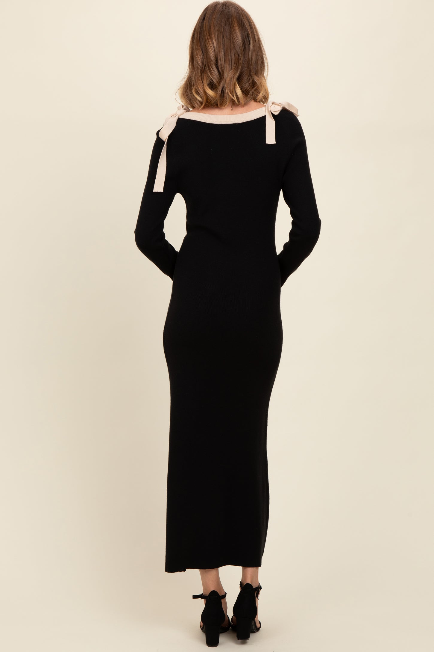woman wearing a black long sleeve maxi dress with light pink bow accents on the shoulders, seen from the back