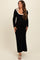 woman wearing a black long sleeve maternity dress with a scooped neckline and a bow detail on the shoulder, showing her baby bump