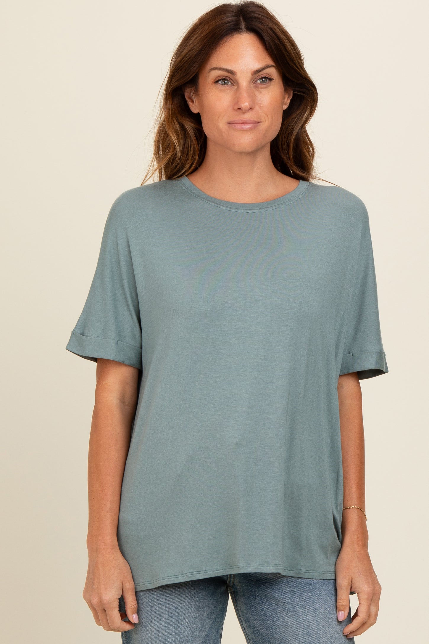 woman wearing a relaxed fit sage green short sleeve top with rolled cuffs and a round neckline