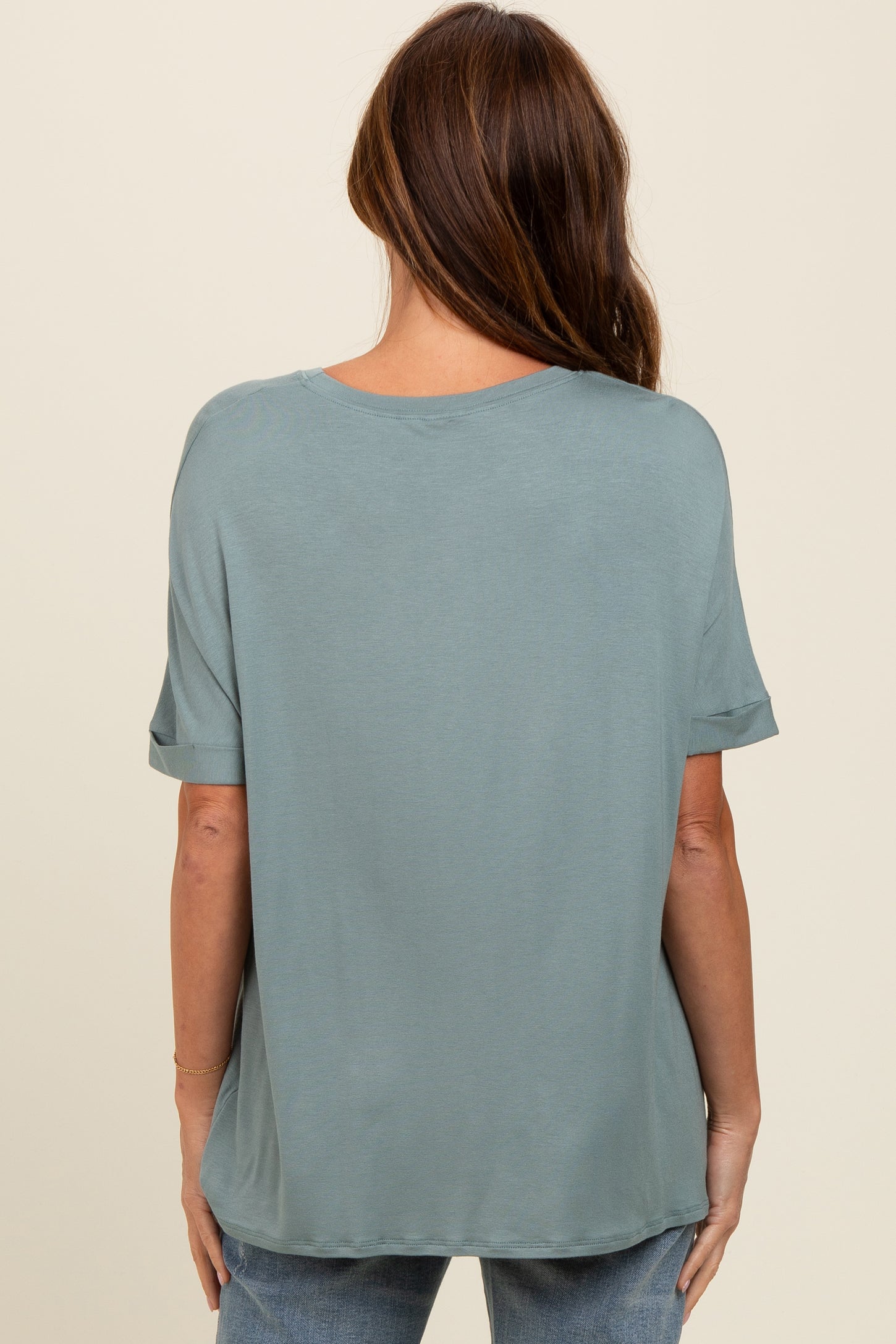 woman wearing a loose-fit sage green short sleeve top, seen from the back