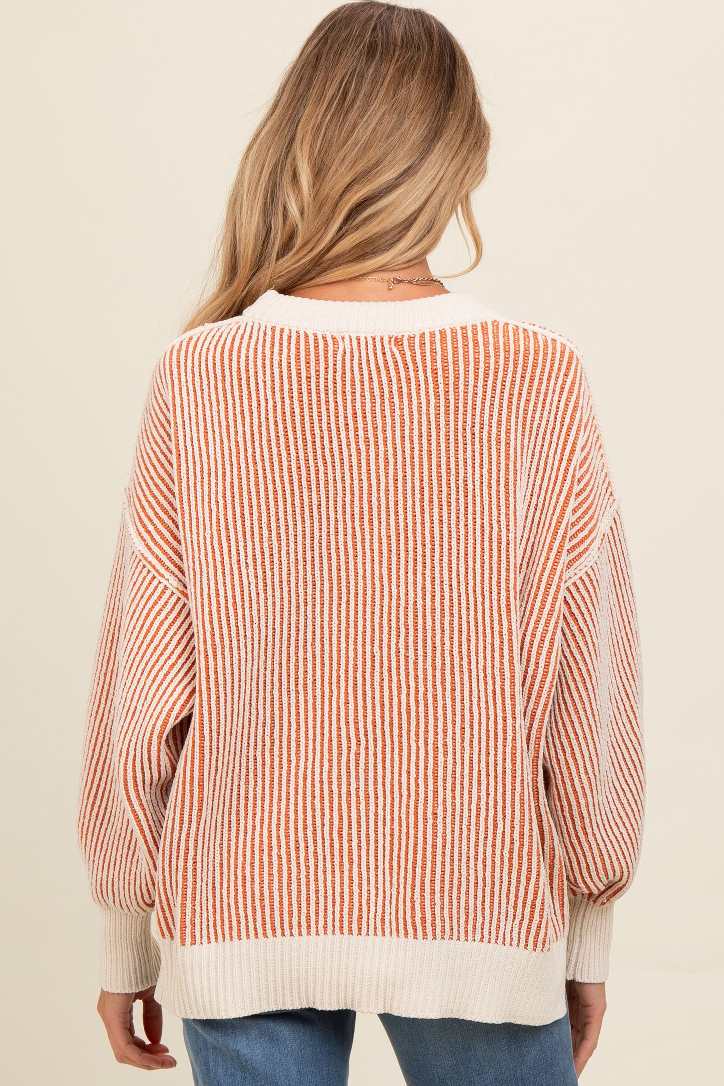 woman wearing a cream and rust striped maternity sweater with a relaxed fit and balloon sleeves, showing the back view