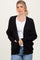 woman wearing a black knitted cardigan over a white top and blue jeans, with hands in pockets and a relaxed expression