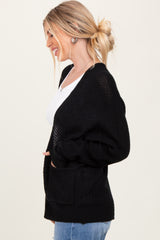 woman wearing a black oversized cardigan with pockets and a white top, smiling and facing sideways