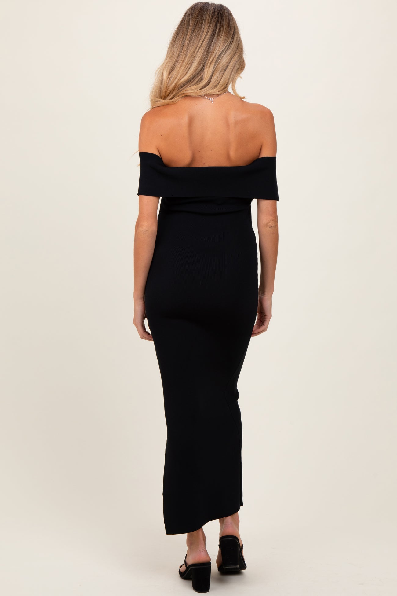 woman wearing a black off-the-shoulder maternity maxi dress, showing the back view with a fitted silhouette