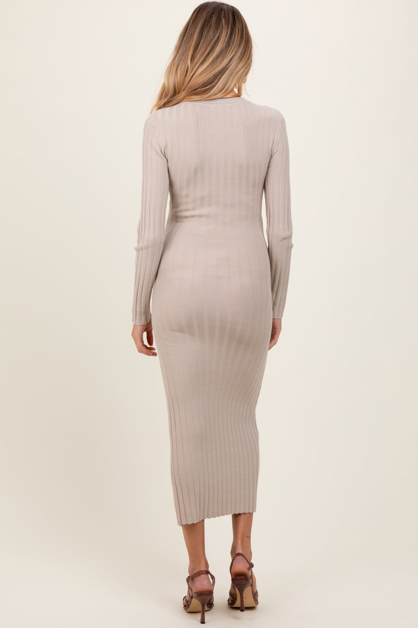 woman wearing a ribbed beige maternity dress with long sleeves and a midi length, showing a subtle baby bump