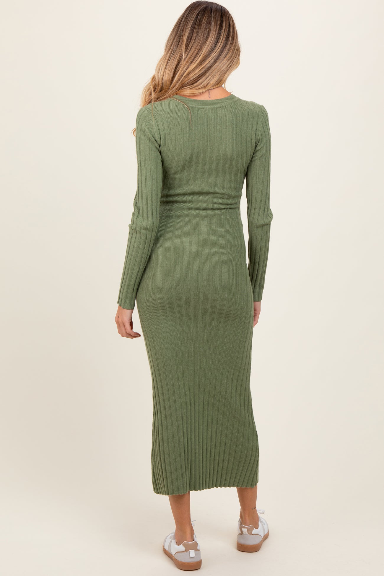 woman wearing an olive green ribbed maternity dress that falls to mid-calf, showing a fitted silhouette and long sleeves