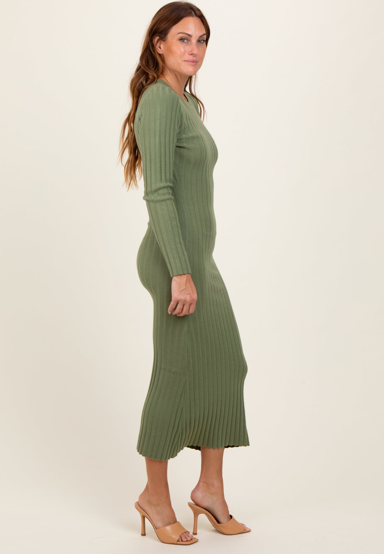 woman wearing a fitted olive green ribbed midi dress with long sleeves and side slits, paired with nude heels