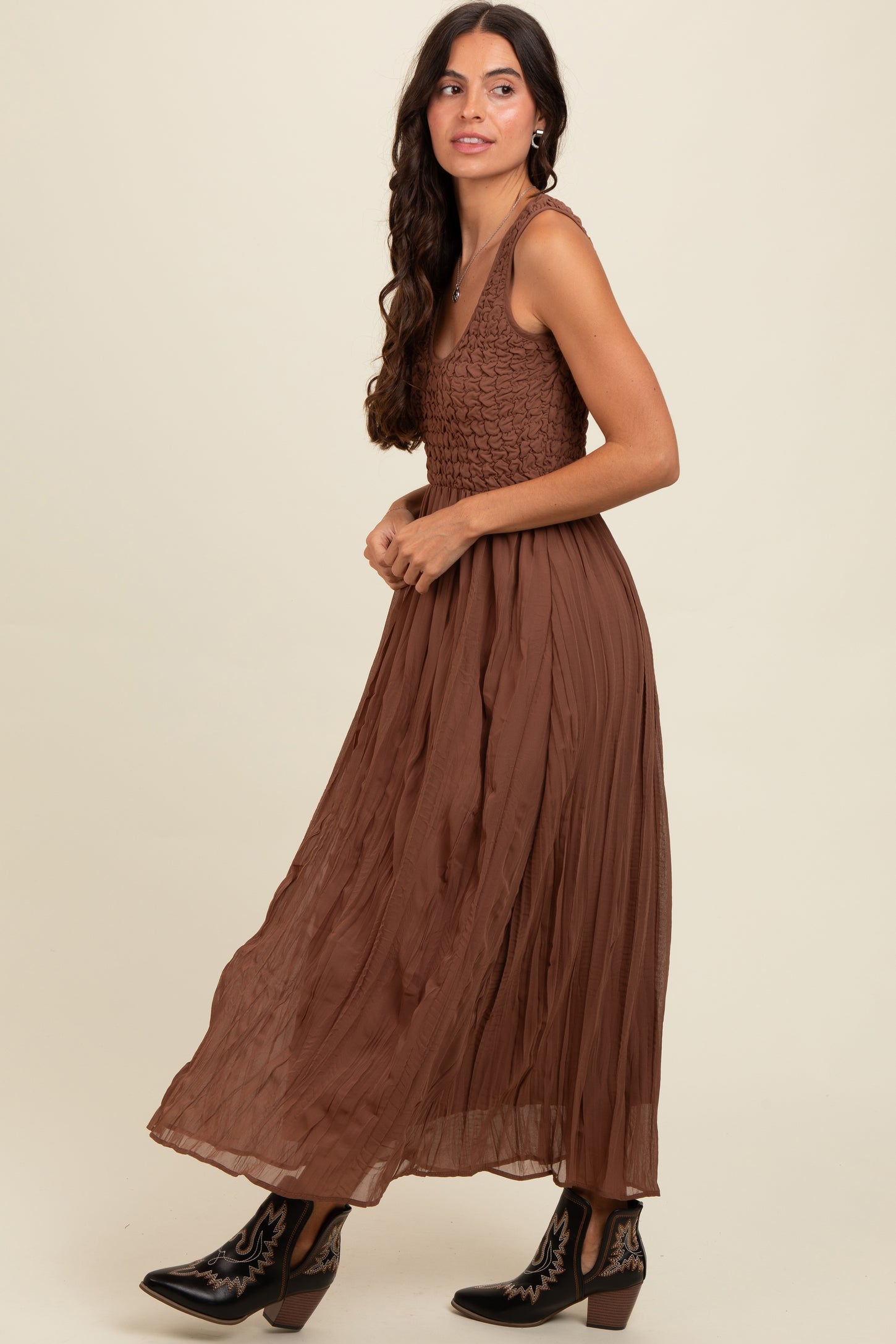 woman wearing a brown maxi dress with a textured bodice and pleated skirt, styled with black western boots