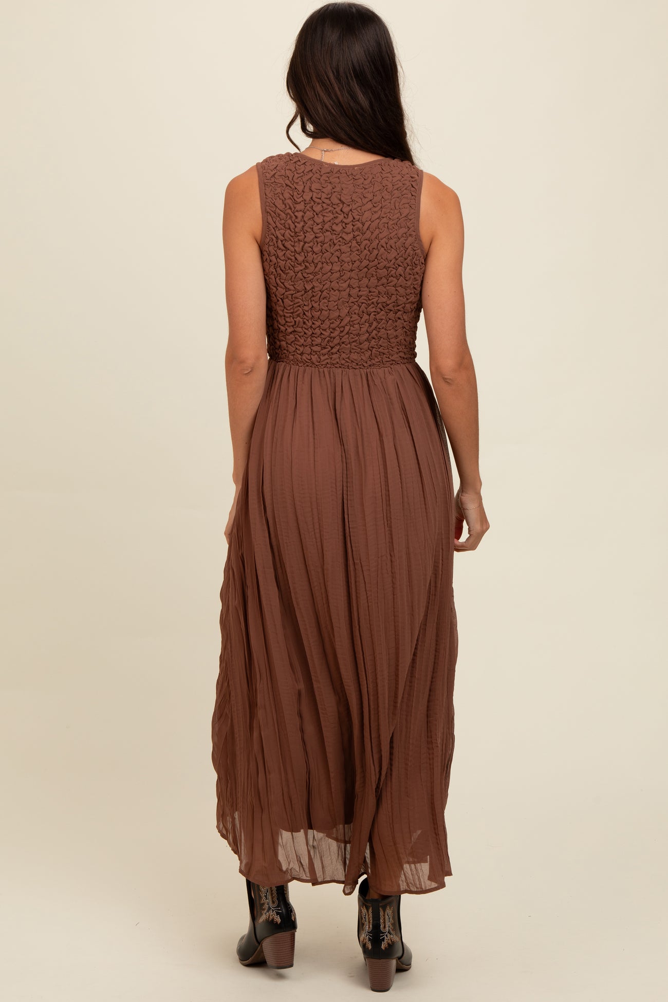 woman wearing a sleeveless brown maxi dress with a smocked bodice and flowing skirt from the back