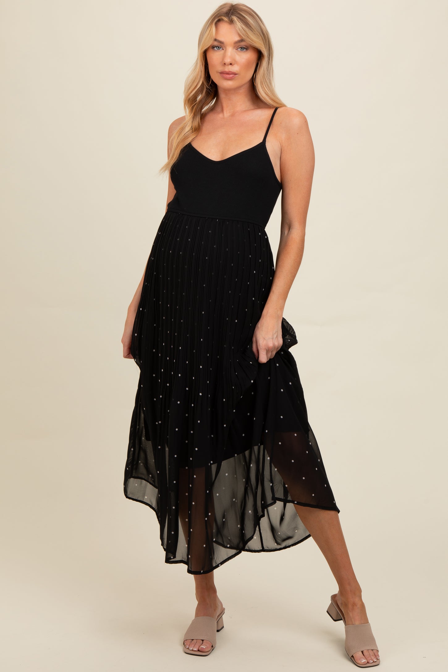 woman wearing a black maternity dress with a flowy skirt and subtle dot details, showcasing her baby bump