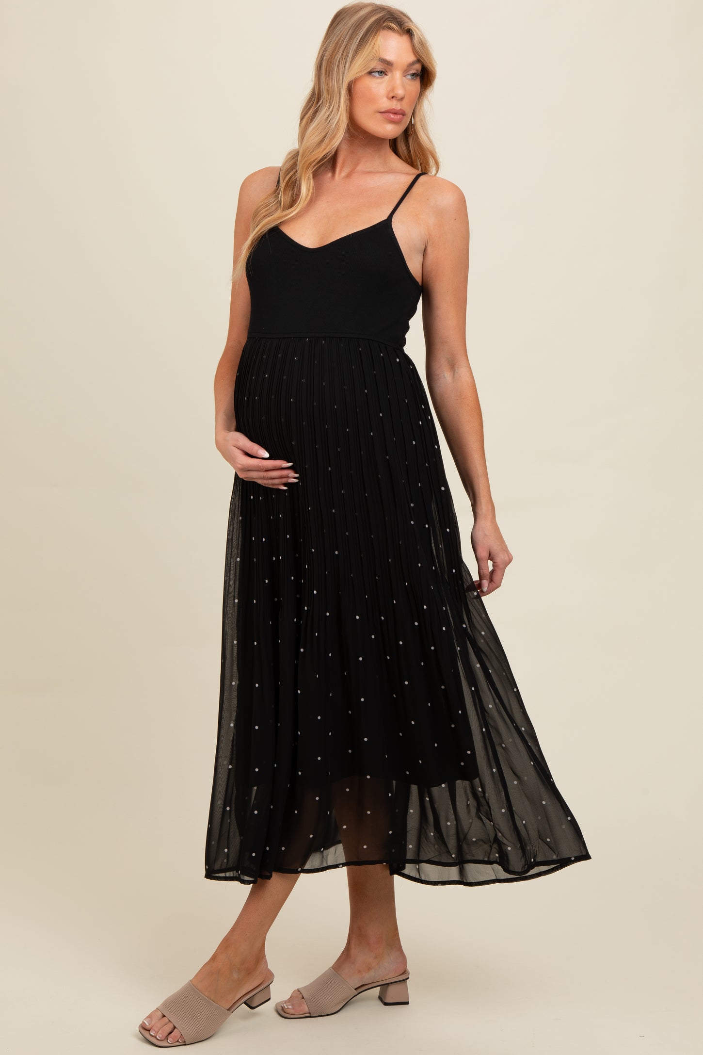 woman wearing a black maternity dress with a pleated skirt and embellished details, showing her baby bump