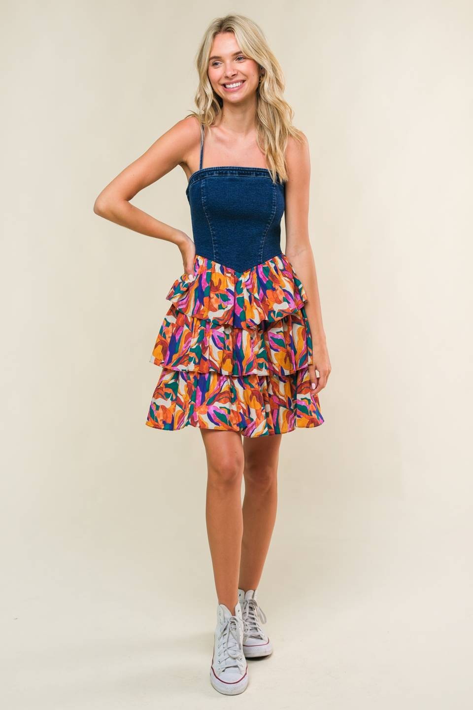 woman wearing a navy denim strapless dress with a colorful layered ruffled skirt and white sneakers