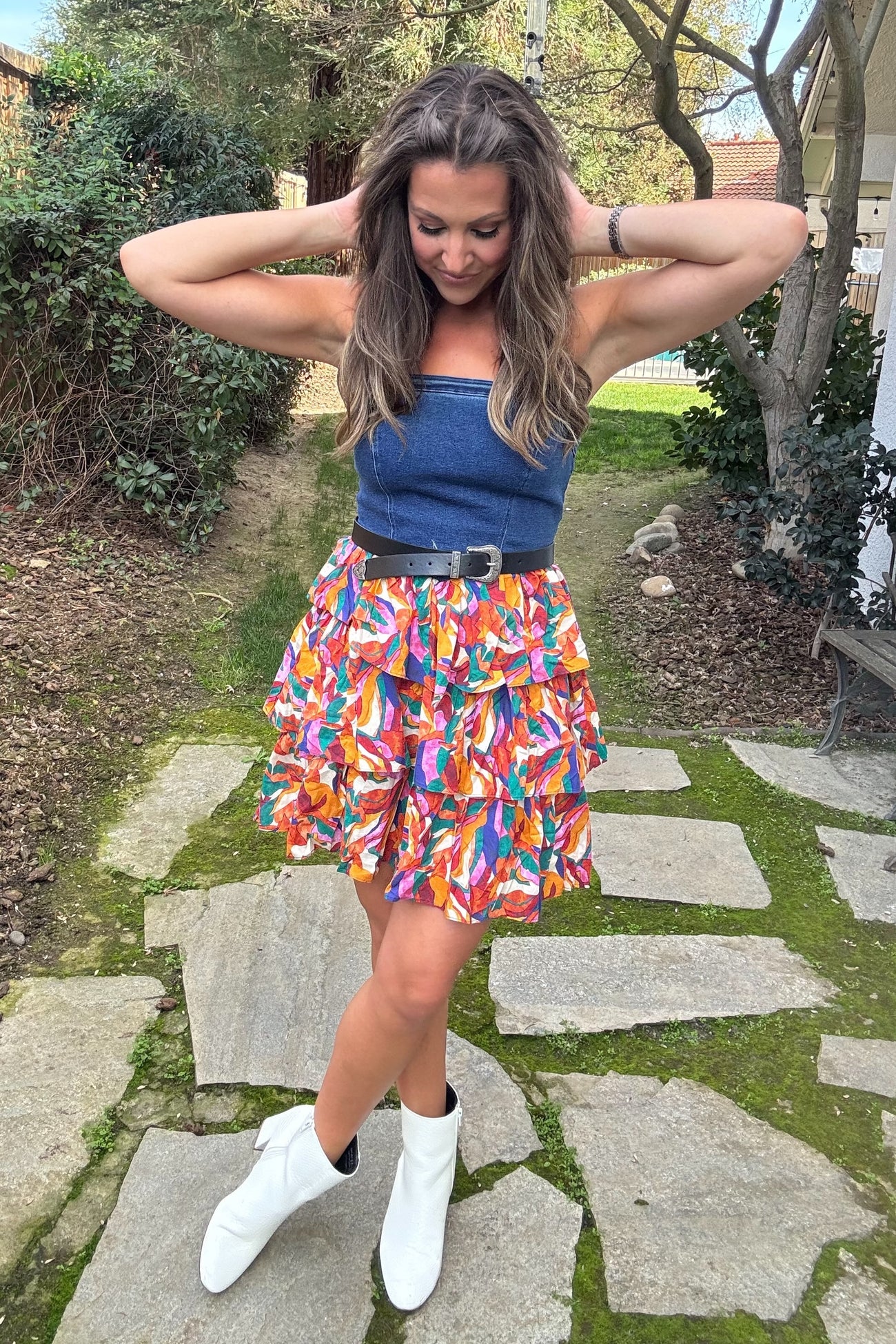 woman wearing a denim strapless top with a colorful tiered mini skirt and white ankle boots, posing outdoors