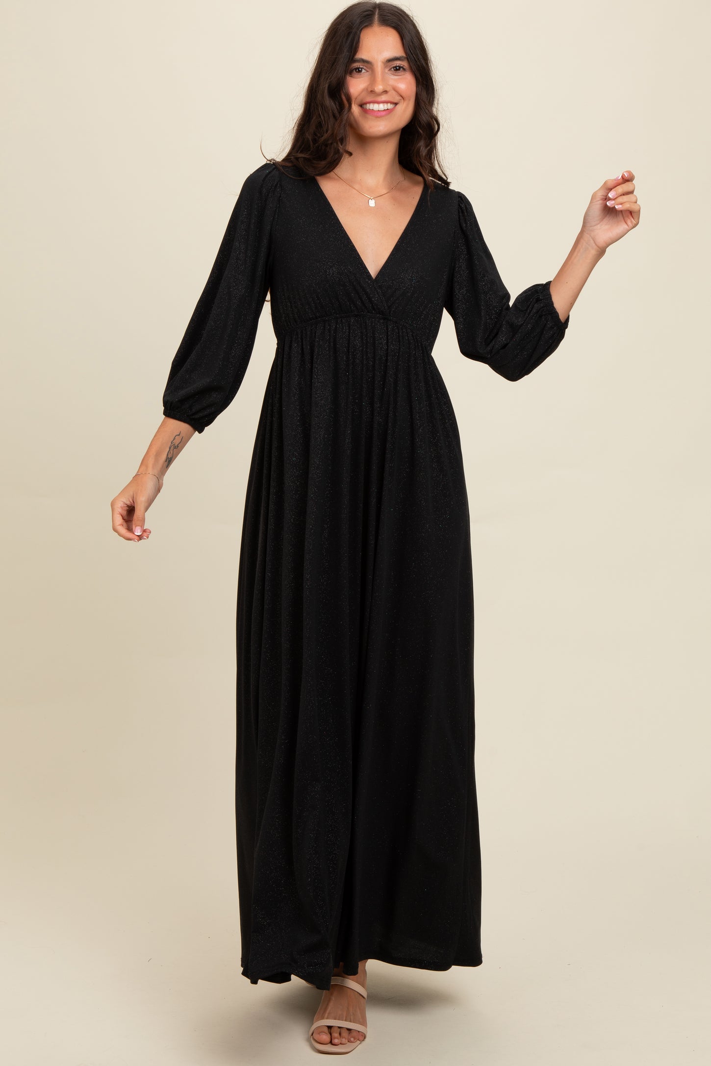 woman wearing a black long sleeve maxi dress with a v-neckline and puffed sleeves, posing with one hand up