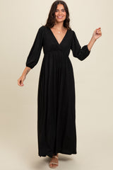 woman wearing a black long sleeve maxi dress with a v-neckline and puffed sleeves, posing with one hand up