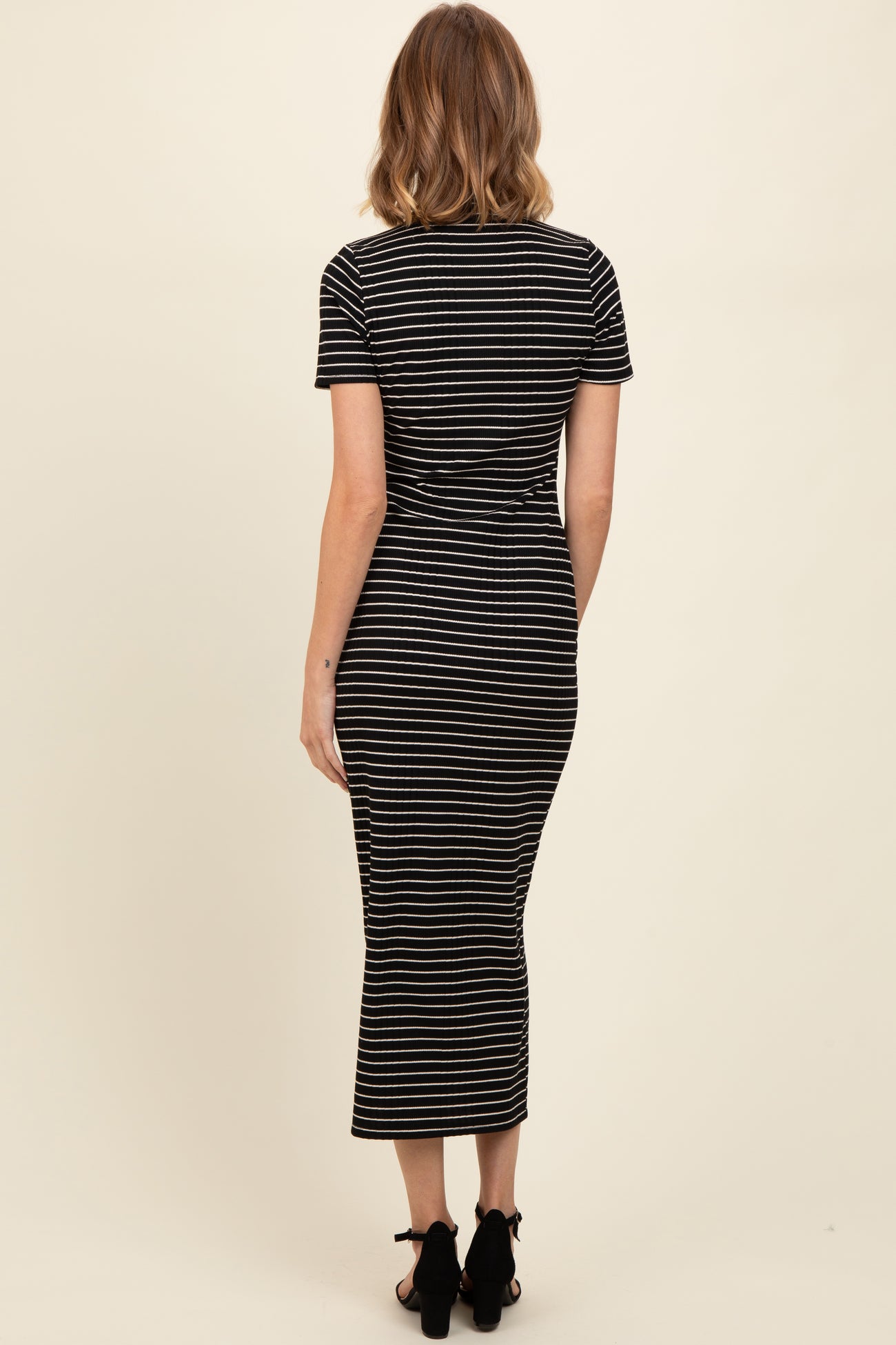 woman wearing a black and white striped fitted midi dress with short sleeves and a scooped neckline, viewed from the back