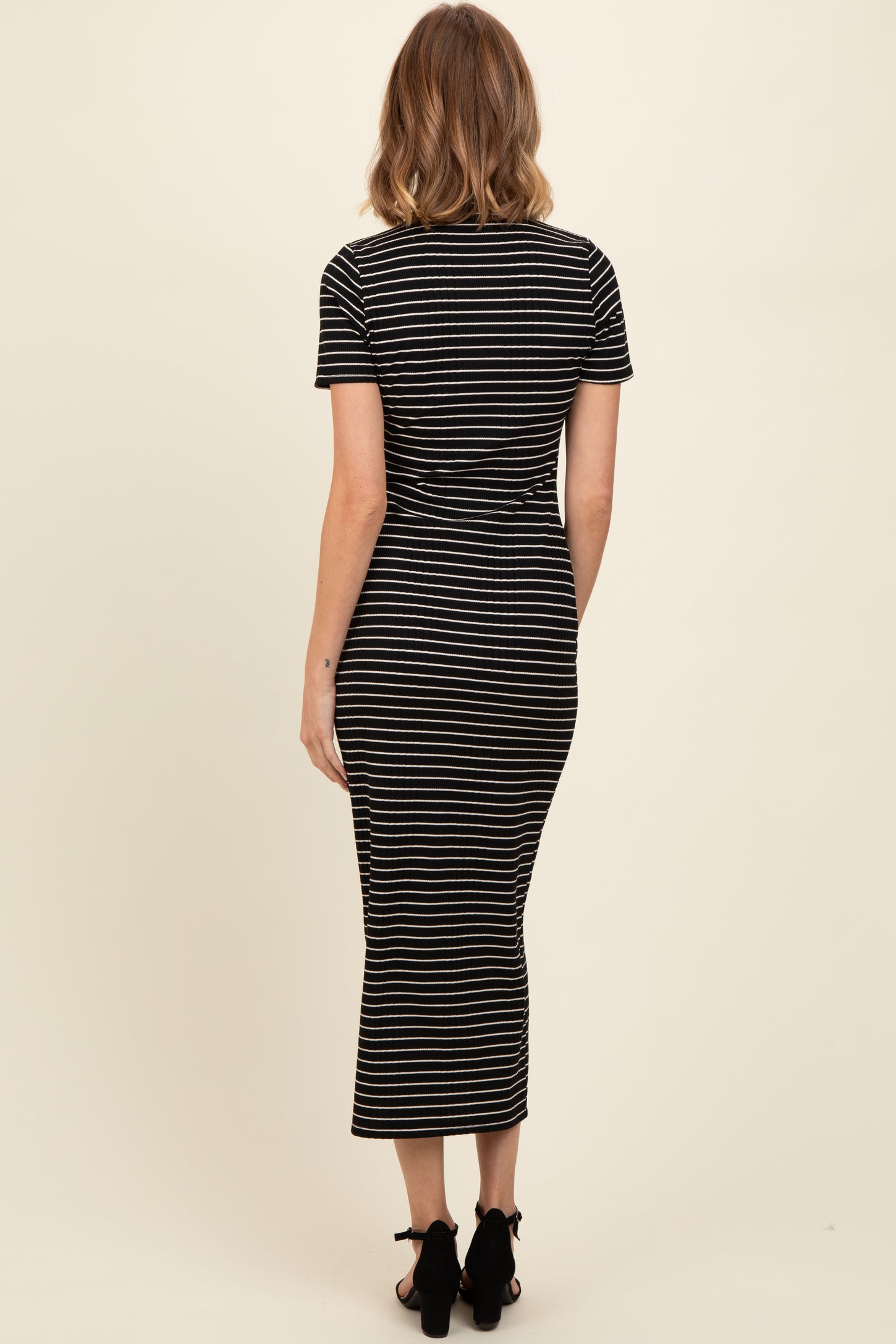 woman wearing a black and white striped fitted midi dress with short sleeves and a scooped neckline, viewed from the back