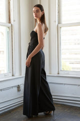 woman wearing a black strapless wide-leg jumpsuit, standing near a window with a modern aesthetic