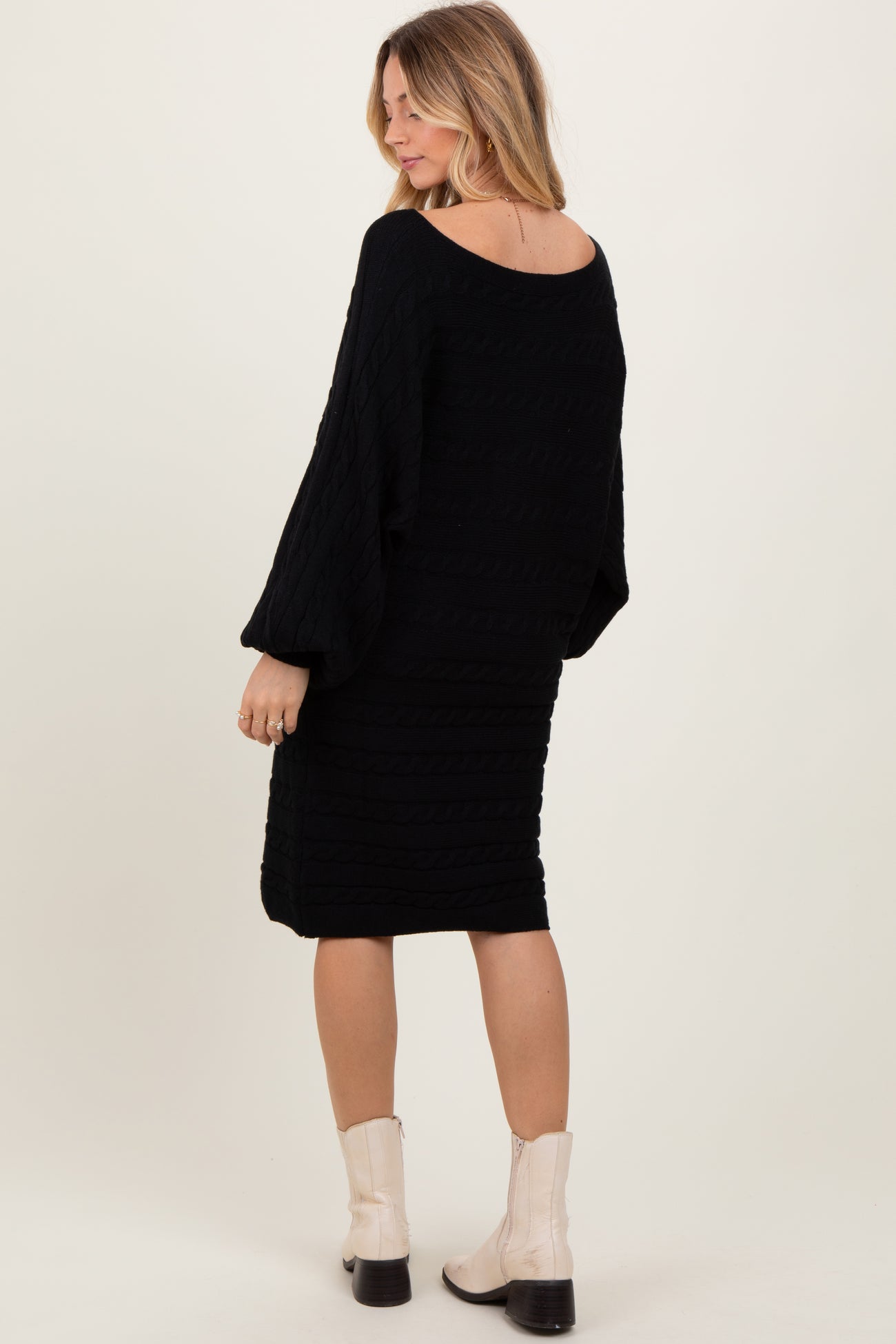woman wearing a black knitted dress with a loose fit and balloon sleeves, styled with light-colored ankle boots