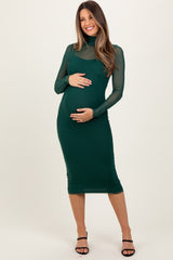 woman wearing a dark green maternity dress with sheer long sleeves and a baby bump