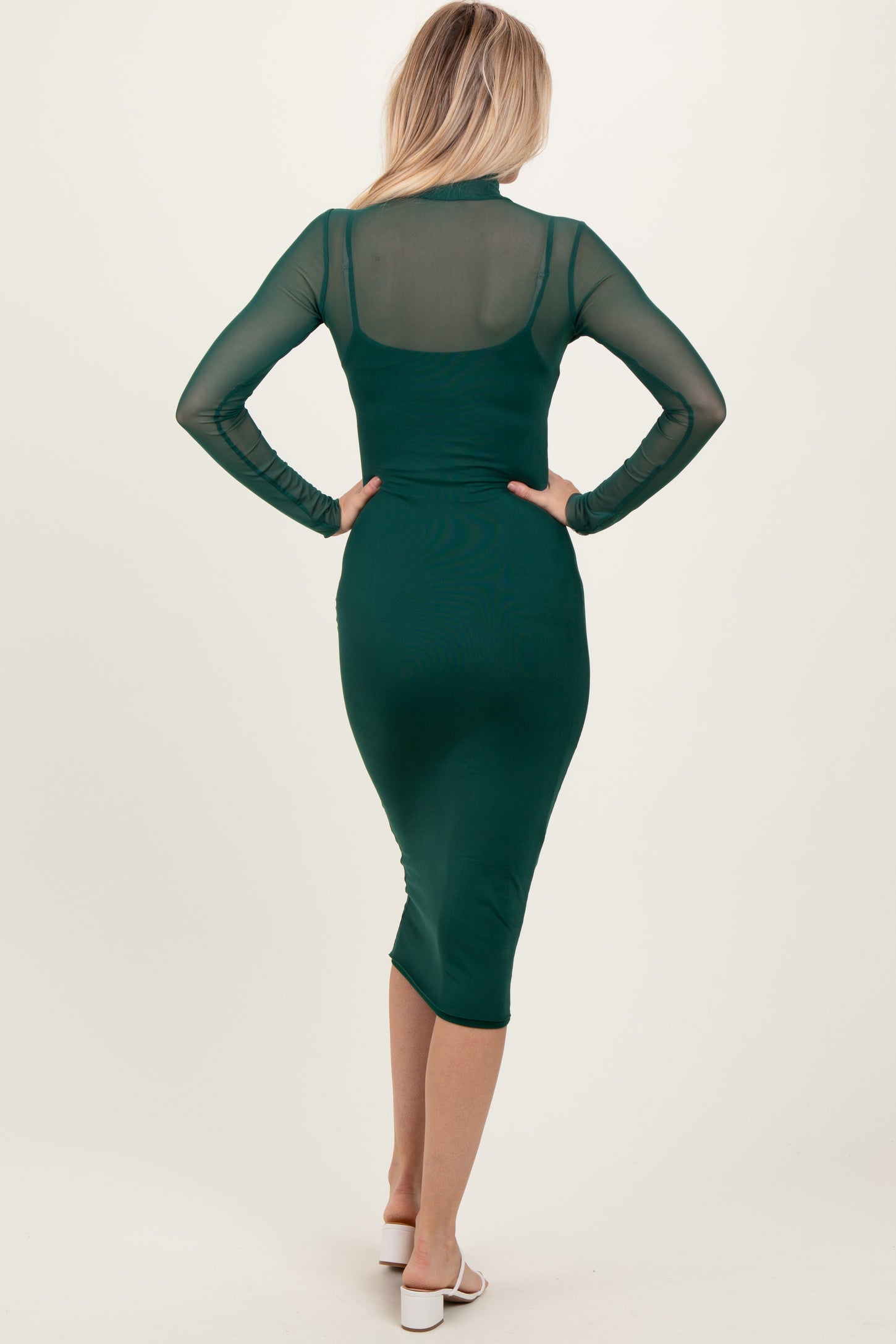 woman wearing a dark green long sleeve bodycon dress with a sheer back and a knee-length hemline