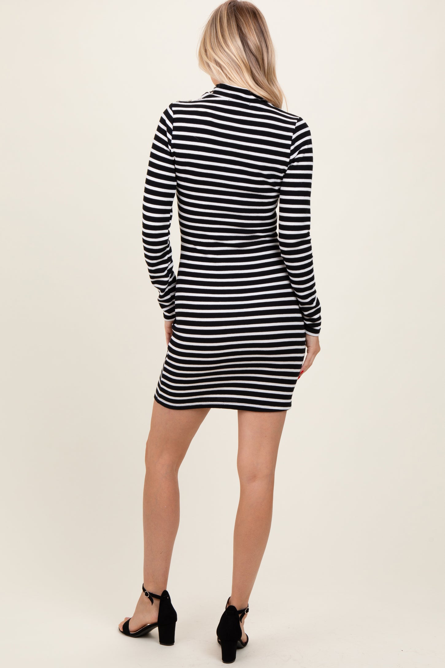woman wearing a black and white striped long sleeve dress, view from the back, paired with black heeled sandals