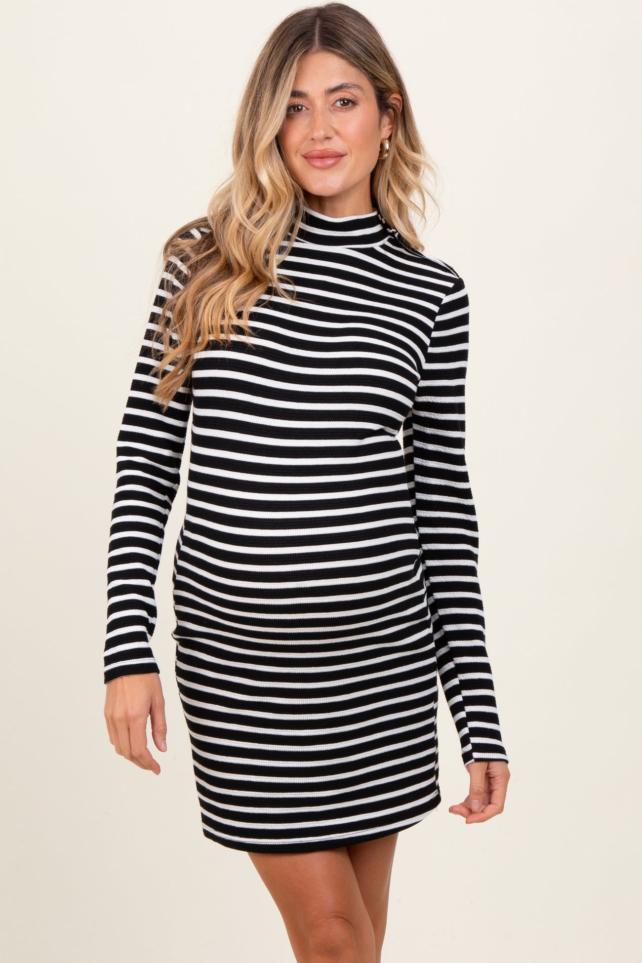 woman wearing a black and white striped maternity dress with a high neck and long sleeves, showing her baby bump