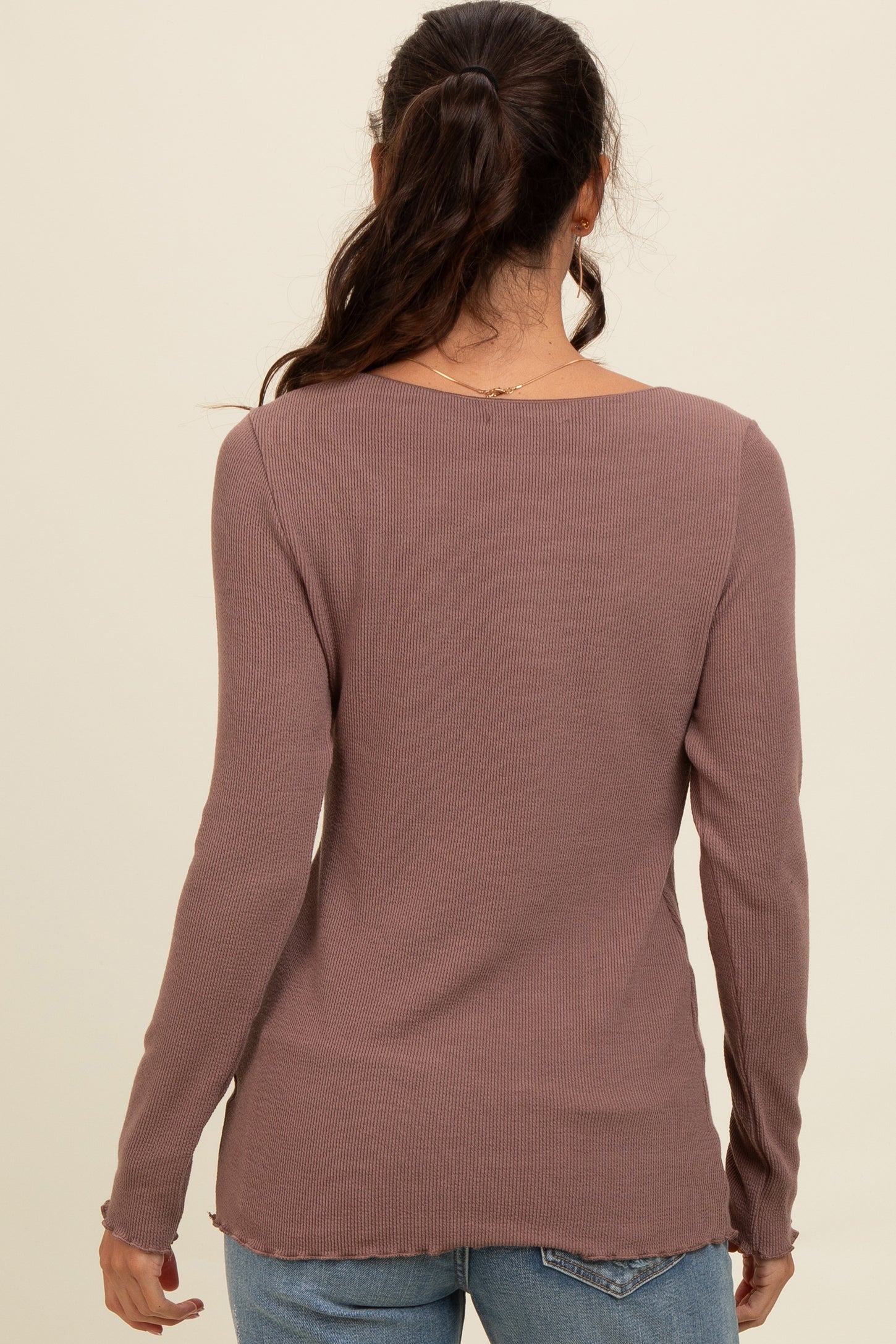 woman wearing a dusty mauve ribbed long sleeve top with a rounded neckline and frayed hem, seen from the back