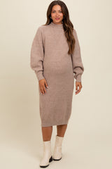 woman wearing a beige knitted maternity dress with a high neck and balloon sleeves, showcasing her baby bump