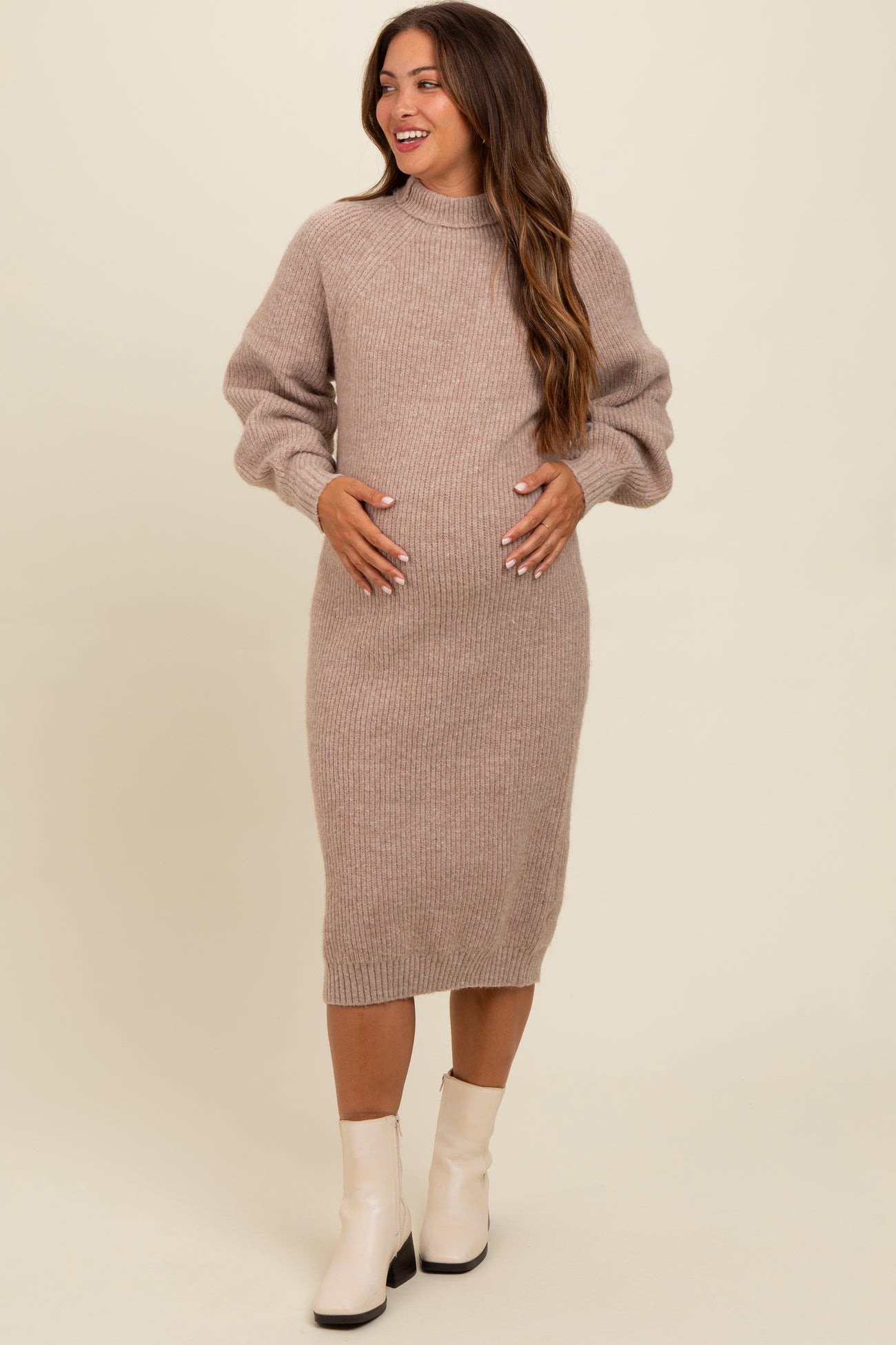 woman wearing a light brown maternity sweater dress with puff sleeves and holding her baby bump