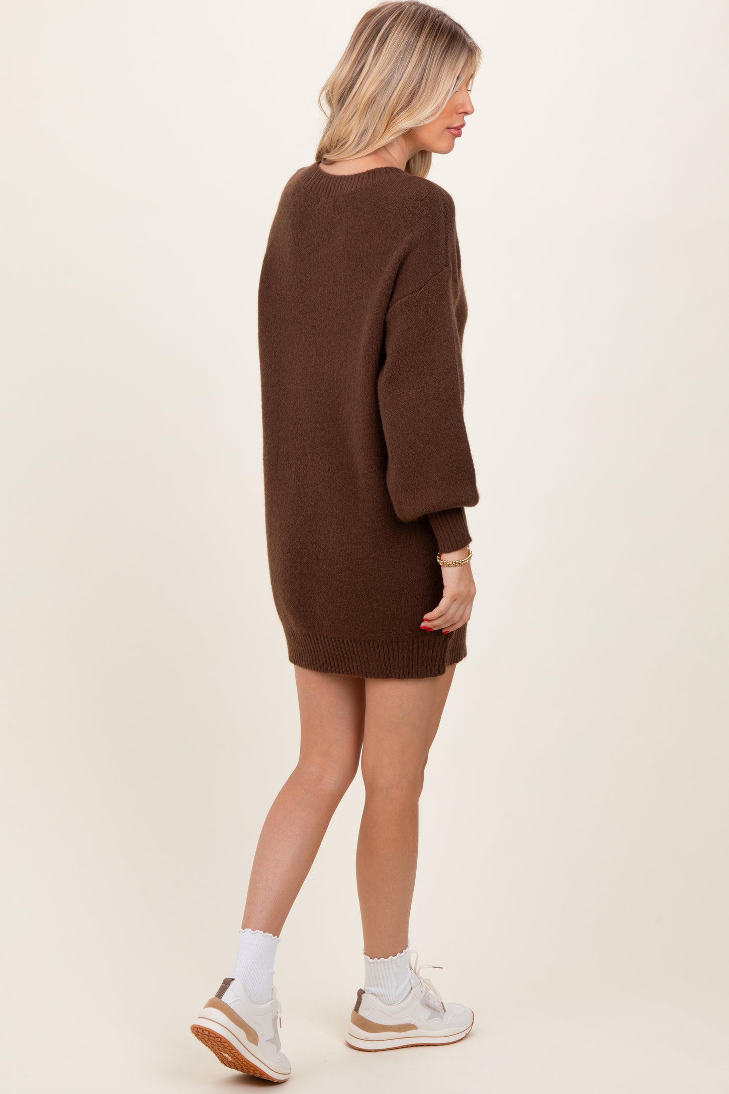 woman wearing a brown oversized sweater dress with balloon sleeves and white sneakers, shown from the back