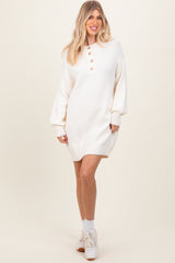 woman wearing a cream oversized sweater dress with button detail and balloon sleeves, paired with white sneakers