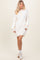 woman wearing a cream oversized sweater dress with button detail and balloon sleeves, paired with white sneakers