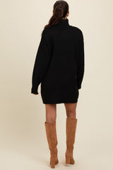 woman wearing a black oversized sweater dress and tan knee-high boots, viewed from the back