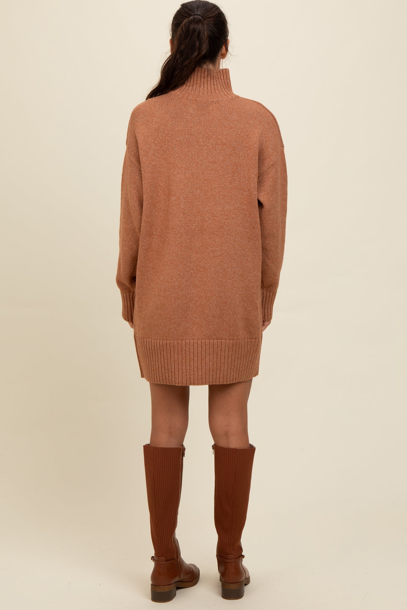 woman wearing a brown oversized sweater dress with a high neck and long sleeves, styled with knee-high brown boots