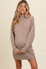 woman wearing a cozy beige maternity sweater dress with oversized sleeves and ribbed detailing, holding her baby bump