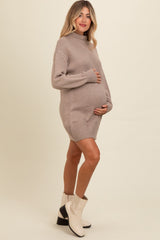 woman wearing a beige maternity sweater dress with a turtleneck and holding her baby bump