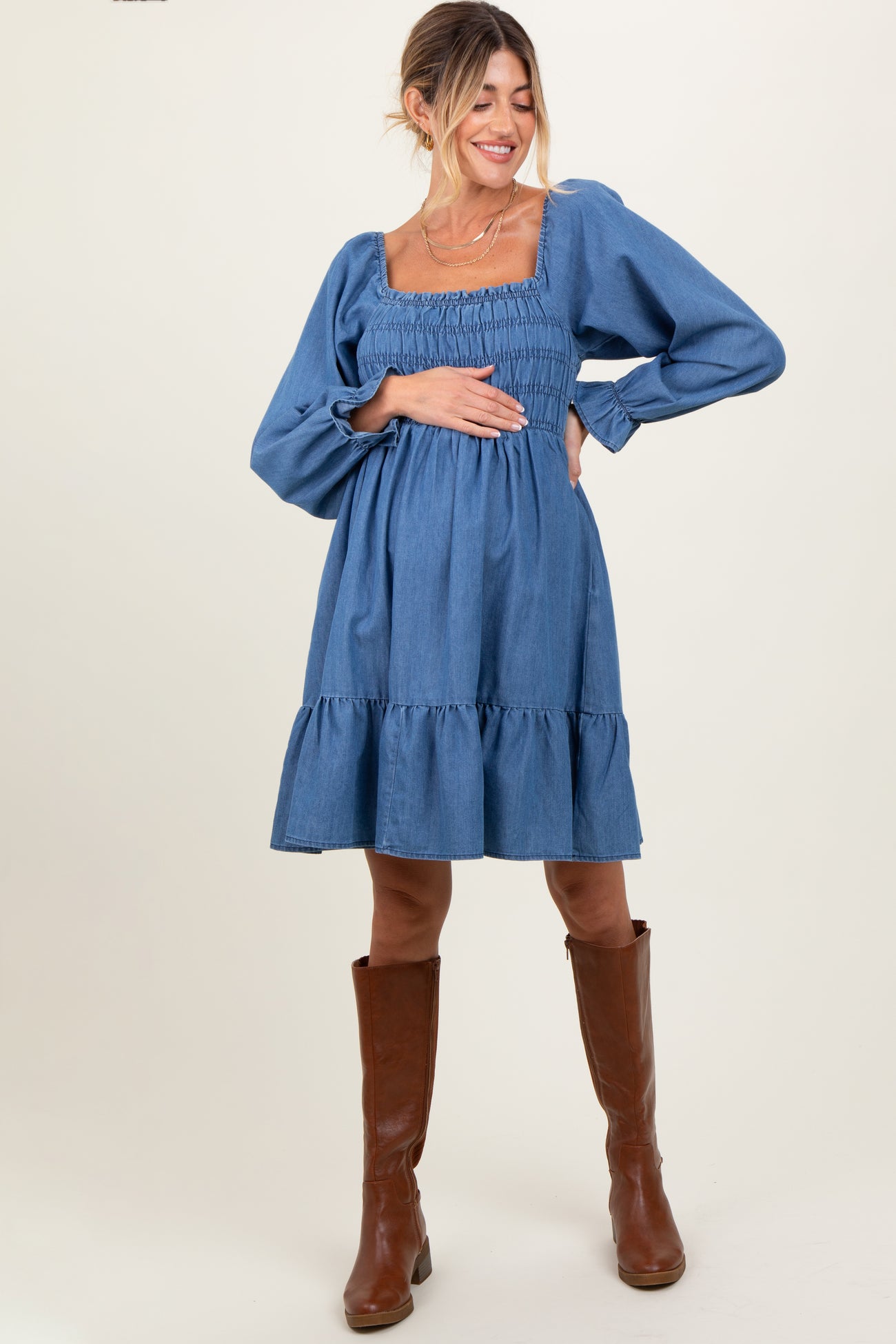 woman wearing a denim blue maternity dress with a square neckline and puff sleeves, holding her baby bump