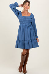 woman wearing a denim maternity dress with smocked bodice and ruffled hem, paired with brown knee-high boots