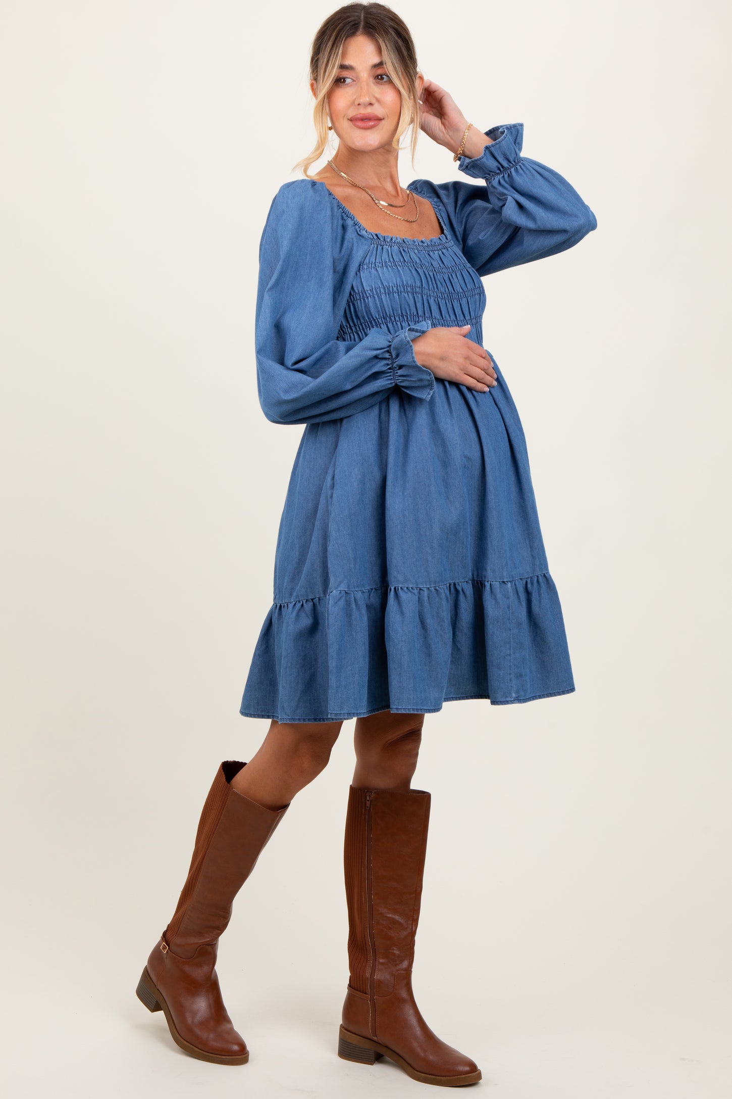 woman wearing a denim smocked maternity dress with a ruffled hem and a visible baby bump
