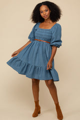 woman wearing a denim smocked square neck dress with a ruffled hem and a tan belt, styled with brown ankle boots