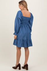 woman wearing a denim smocked dress with long sleeves and a ruffled hem, showing the back view